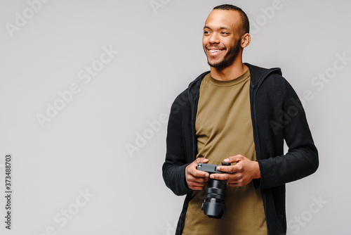 Handsome african american guy holding digital camera over light gray background