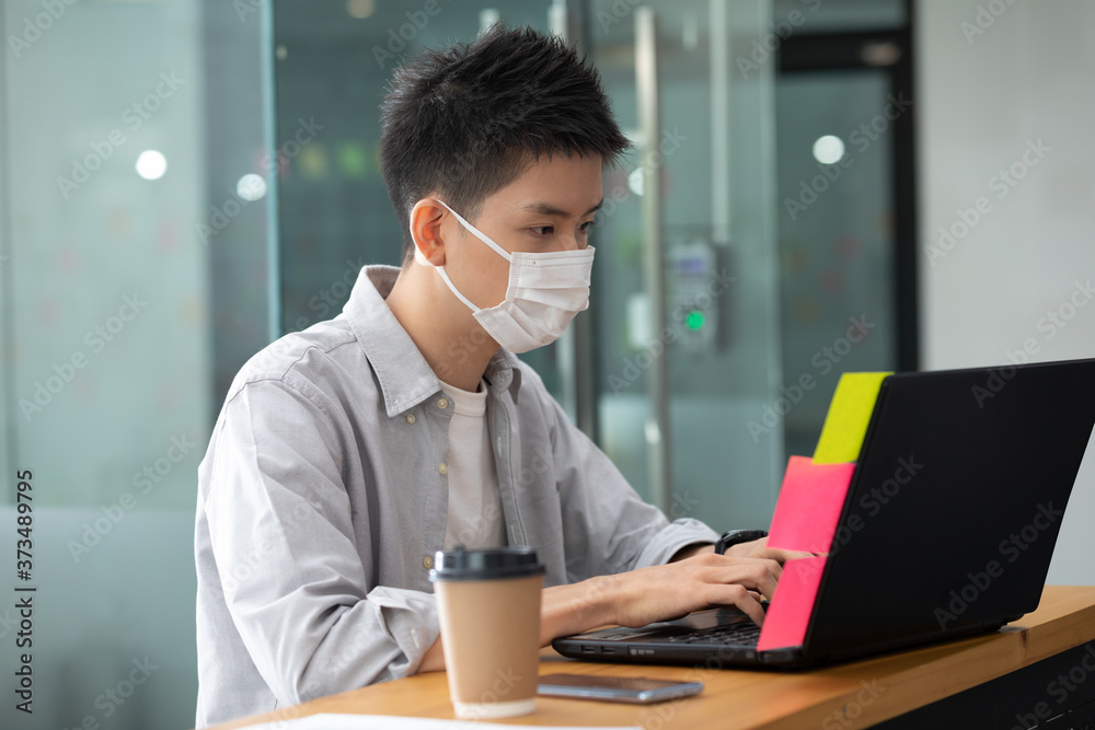 Asian young business man in casual wearing mask working with laptop in modern office or co-working space Due Covid-19 Flu Pandemic,Health care and Business Startup Concept Asian young business man in casual wearing mask working with laptop in modern office or co-working space Due Covid-19 Flu Pandemic,Health care and Business Startup Concept