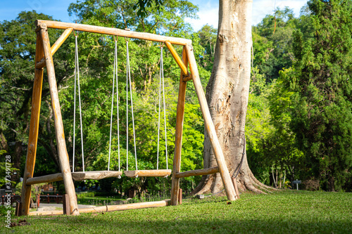 A wooden swing for couple seat in the backyard garden with greenery natural environment in day time. Outdoor object photo. © Nattawit