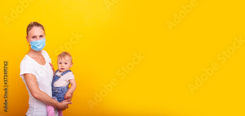 Mutter mit Mundschutz hält ihre Tochter vor gelben Hintergrund auf dem Arm © Mediaparts