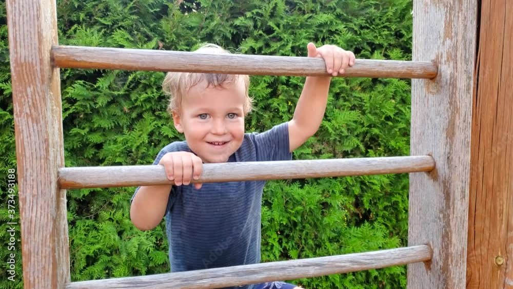 Cute adorable caucasian little toddler brave boy enjoy having fun climbing up wooden stairs at outdoor yard playground. Happy courage child playing with sport ladder at garden outside home Cute adorable caucasian little toddler brave boy enjoy having fun climbing up wooden stairs at outdoor yard playground. Happy courage child playing with sport ladder at garden outside home