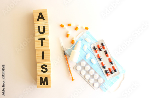 The words AUTISM is made of wooden cubes on a white background with medical drugs and medical mask. Medical concept.
