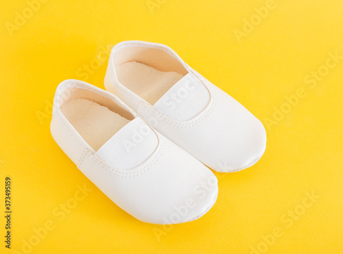 White gym shoes for children on a yellow background. Concepts for comfortable and light indoor shoes and sports, ballet shoes