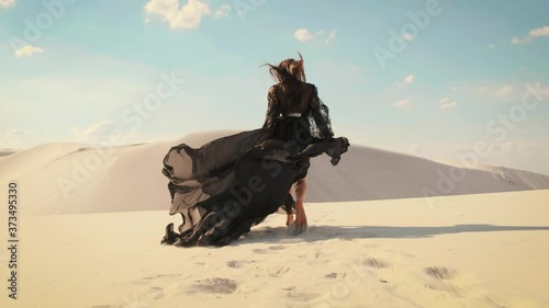 Silhouette of a happy woman running in the desert. Long black silk dress and hair flying fluttering in the wind in slow motion. A tourist is enjoying a vacation in the Dubai desert. Video footage 4K
