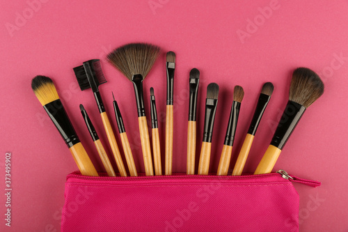 set of makeup brushes in a pink cosmetic bag top view on pink background. concept of make up artist.