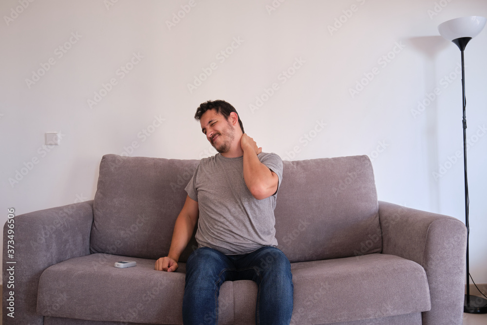 Young man sitting on a sofa suffering from neck pain. Neck and shoulder paint. Young man sitting on a sofa suffering from neck pain. Neck and shoulder paint.