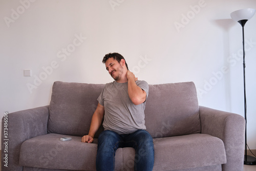 Young man sitting on a sofa suffering from neck pain. Neck and shoulder paint.