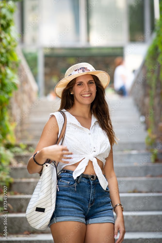 Attractive young girl smiling with a hat and a bag going down the stairs in a park
