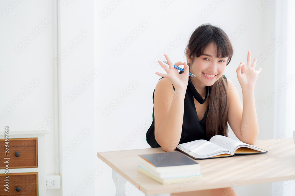 Beautiful portrait young asian woman smiling sitting study and learning writing notebook and diary in the living room at home, girl homework, business woman working on table, education concept.