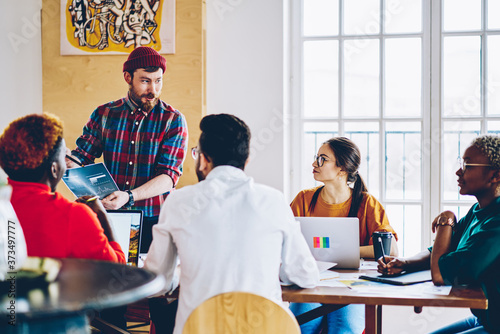 Group of male and female colleagues sitting at desktop analyzing infographic diagrams preparing to finance exams together, hipster guys discussing ideas during gather cooperation on startup project