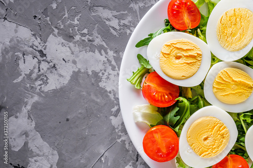 salad with boiled chicken eggs and cherry tomatoes on a stone background