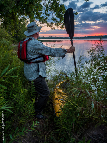 Man holding kayak paddle at shoreline

 photo