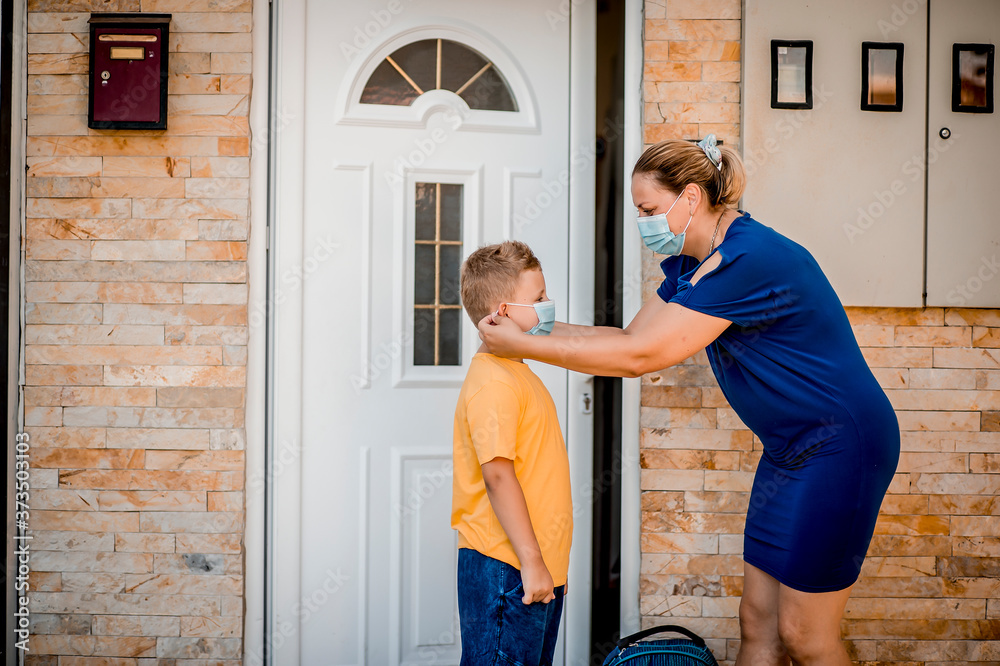 Woman helping her son to be ready to go back to school. They are wearing a protective face mask Woman helping her son to be ready to go back to school. They are wearing a protective face mask