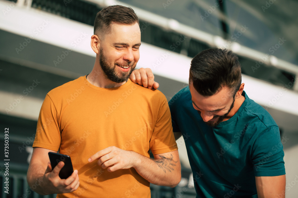 Two happy excited fan friends in euphoria mood after winning in a bet with a smartphone in hand on stadion background Two happy excited fan friends in euphoria mood after winning in a bet with a smartphone in hand on stadion background