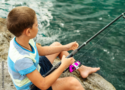 Little boy with fishing rod sitting at the beach