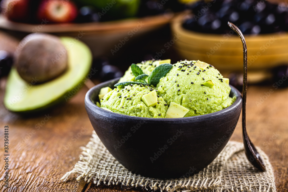 vegan avocado ice cream, without preservatives or added milk. With tropical fruits in the background, in handmade clay bowl.