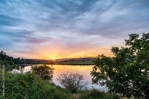 Fototapeta Naklejka Na Ścianę i Meble -  Ausblick über einem See zum Sonnenuntergang am Horizont