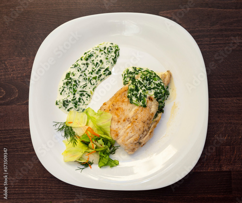 baked chicken breast drizzled with cream sauce with herbs and salad on a white plate on a wooden surface. Healthy food. Top view