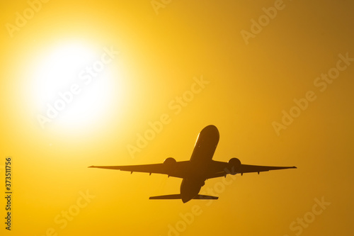 Silhouette of a taking off airliner at sunset next to the bright sun.