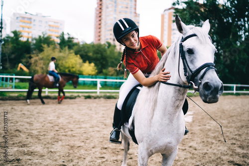 Female equestrian in black helmet caressing horse in paddock