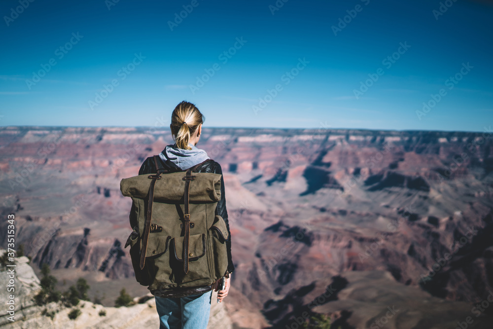 Back view of female traveler with backpack exploring mountains on wanderlust getaway tour looking at high mountains, woman tourist enjoying scenery of rocks valley getting to destination in journey Back view of female traveler with backpack exploring mountains on wanderlust getaway tour looking at high mountains, woman tourist enjoying scenery of rocks valley getting to destination in journey