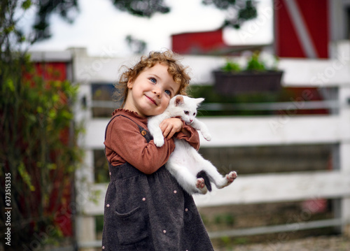 Small girl with cat standing on farm, looking at camera.