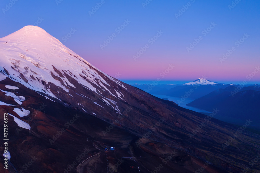 aerial photo from high altitude of the snowy summit of the volcano osorno in the blue hour. In the background the Todos los Santos lake and the Tronador hill