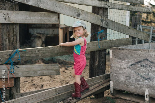 A young girl stands on a fence wearing a leotard and cowgirl boots. photo