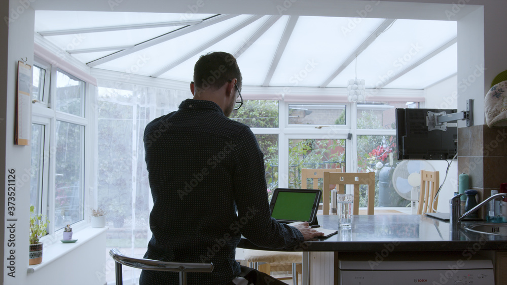 Male professional using a green screen tablet while working from home in a kitchen Male professional using a green screen tablet while working from home in a kitchen