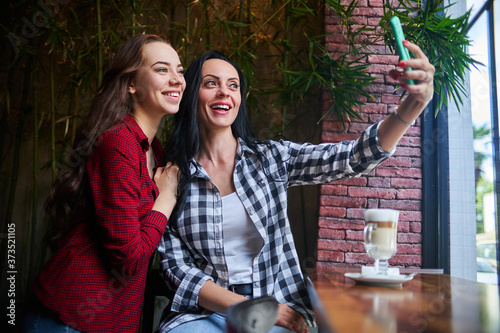 Casual happy smiling joyful mother and daughter taking a selfie photo on a phone camera and having good time together in a coffee shop