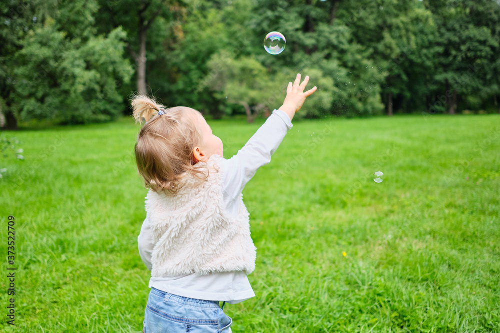 Caucasian kid runs in the park in the summer for soap bubbles Caucasian kid runs in the park in the summer for soap bubbles