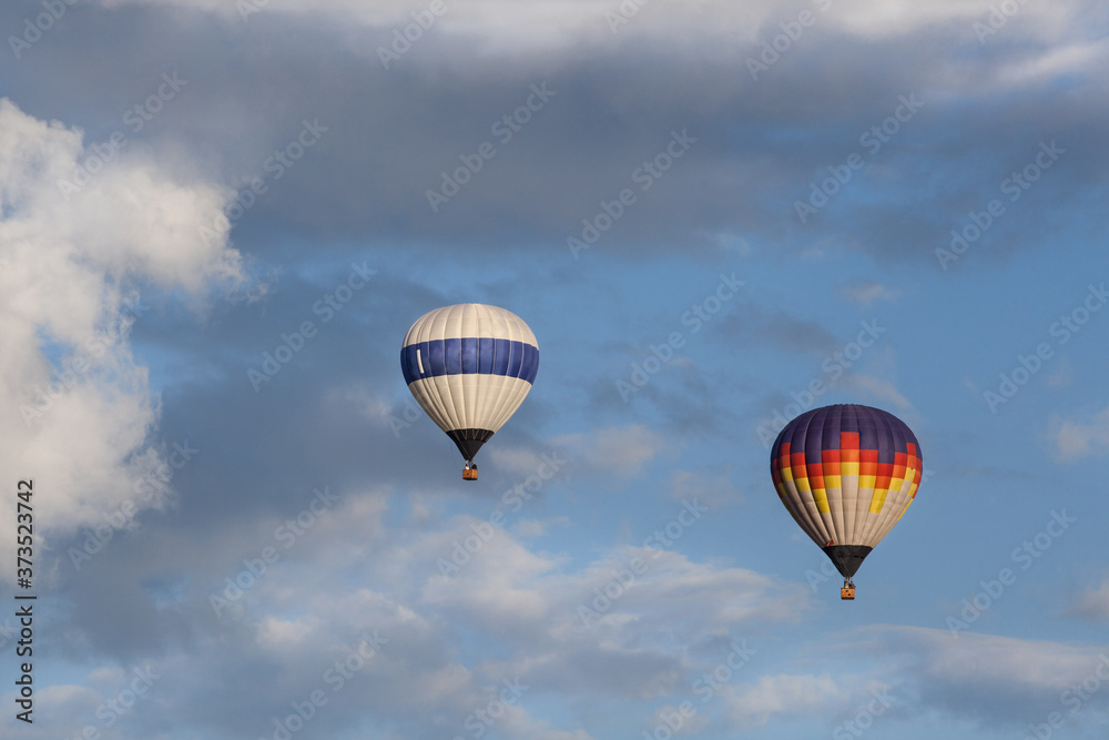 Naklejka premium Two multi-colored hot air balloons flying in the sky. Some clouds in the sky. 