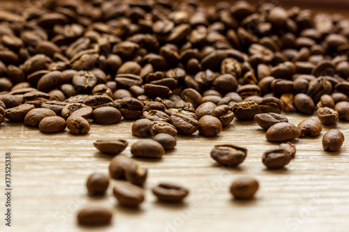 Roasted arabica coffee beans, in bulk on a wooden table.