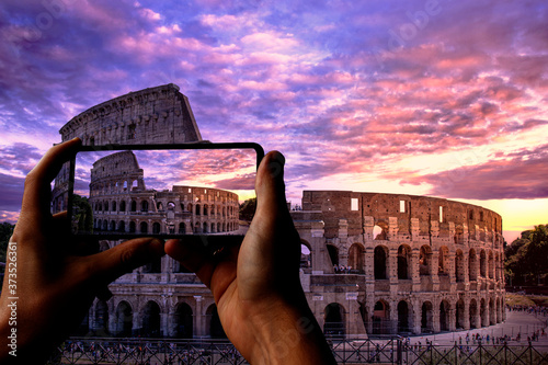 Photography Tourist taking photo of Colosseum (Coliseum) in Rome at sunset against purple cloudy sky, Italy