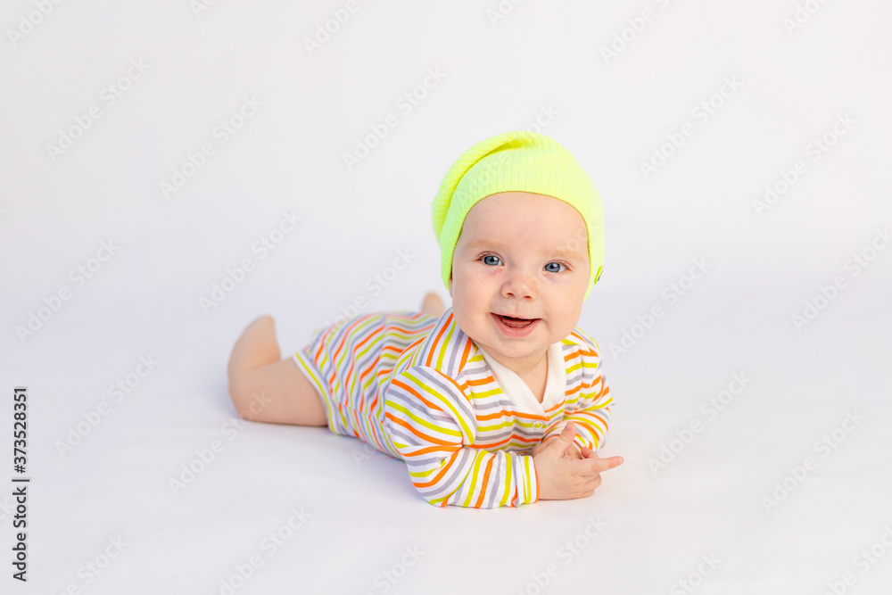 small smiling baby girl 6 months old lies on a white isolated background in a bright bodysuit and yellow hat, space for text