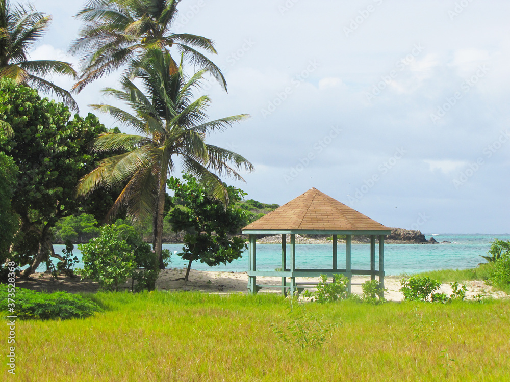 Plage tropicale de sable fin aux eaux turquoises,avec palmiers et petit kiosque hexagonal servant d'abri pour les vacanciers