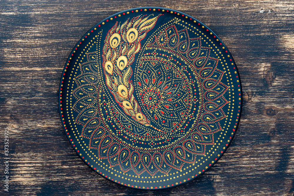 Decorative ceramic plate with black, red and golden colors, painted plate on wooden background , dot painting - obrazy, fototapety, plakaty 