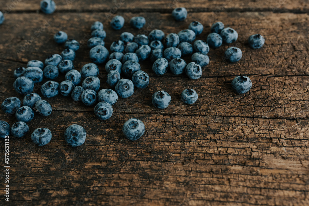 Blue fresh blueberries are scattered on an old brown wooden cracked table. Blue fresh blueberries are scattered on an old brown wooden cracked table.