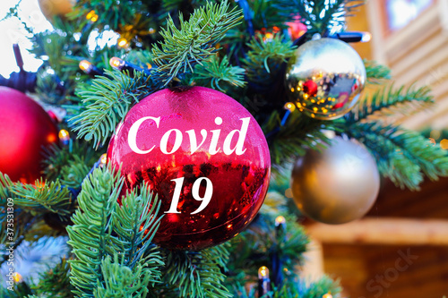 View on red glitter ball on fir tree with covid 19 text at christmas market