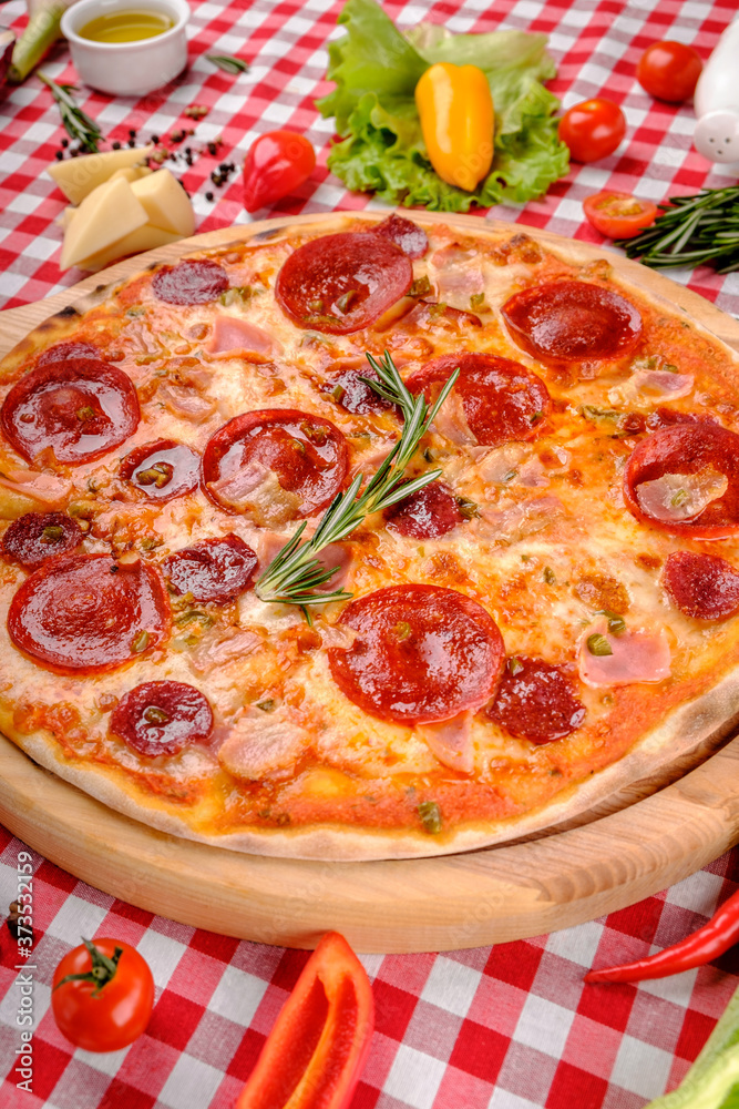Neapolitan Pepperoni pizza with sausage, salami, cheese, rosemary and tomatoes sauce, served on a wooden board for a dinner in italian restaurant background, top view.