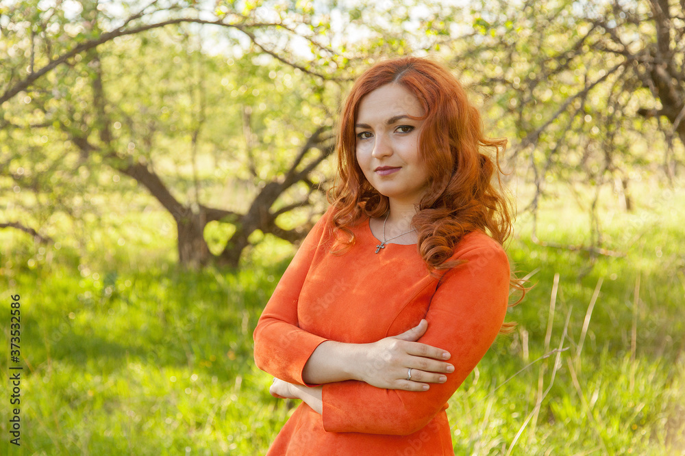 Portrait of a red-haired girl walking in an apple orchard in an orange dress Portrait of a red-haired girl walking in an apple orchard in an orange dress