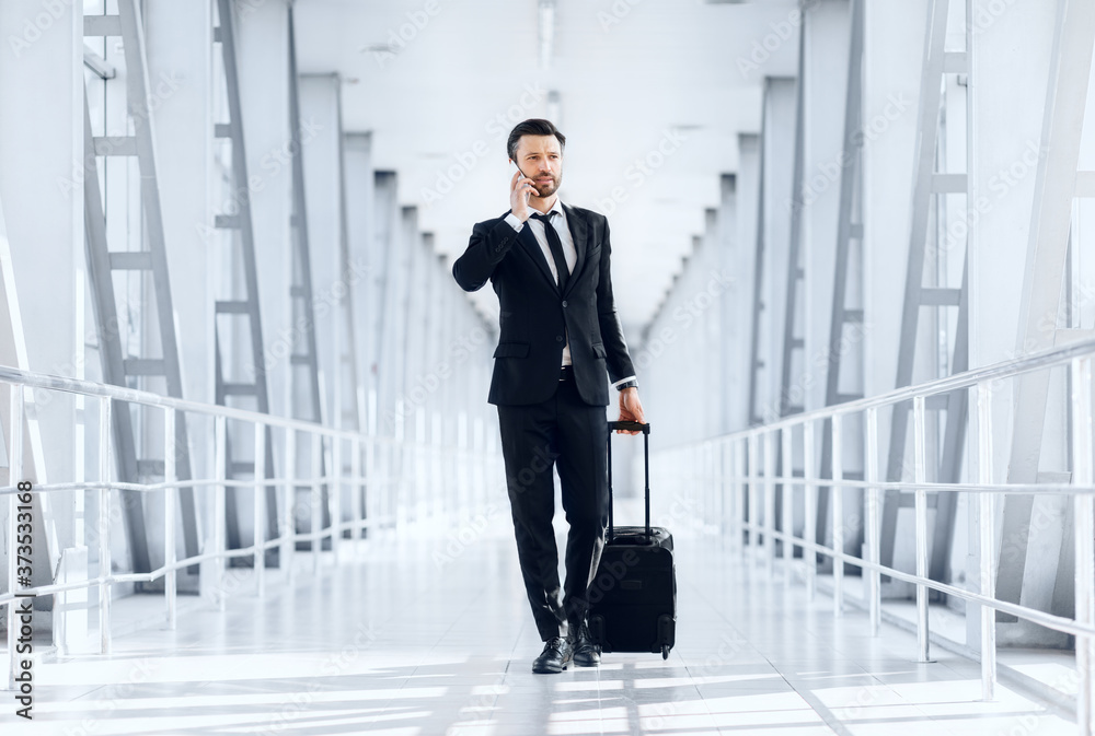 Young businessman talking on phone, walking with luggage in airport Young businessman talking on phone, walking with luggage in airport