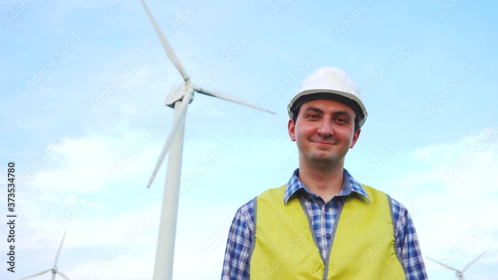 Engineer smiling, looking at camera in front of wind turbines ecological energy industry power windmill Engineer smiling, looking at camera in front of wind turbines ecological energy industry power windmill
