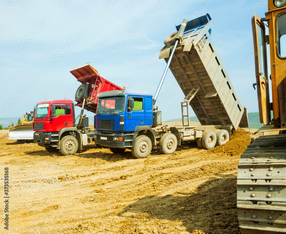 On-board dump trucks unload sand into a ravine, after which bulldozers rake up the rest of the earth.