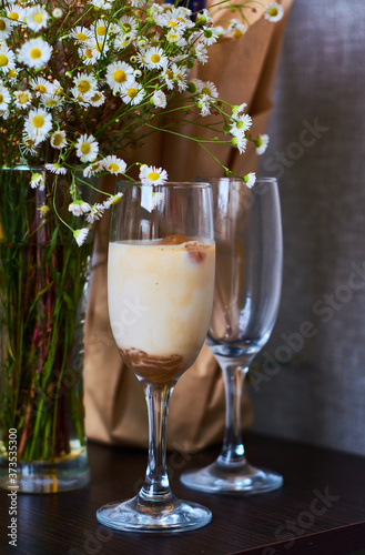 Cold latte, coffee with milk and ice in beautiful glass on dark background with small flowers daisy.