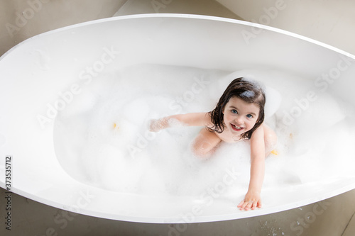 High angle view of smiling toddler girl taking bath in bathtub