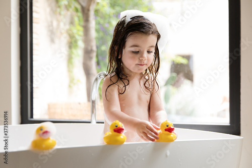 Toddler girl playing with rubber ducks in bathtub