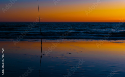 Fishing rod stuck in the sand on the beach, waiting for a fish to bite as the sun goes down