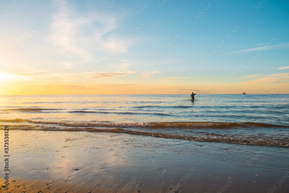 Beautiful landscape view of nature in the morning sunrise with silhouette fisherman on the beach and orange sunlight blue sky background at huahin in Thailand 