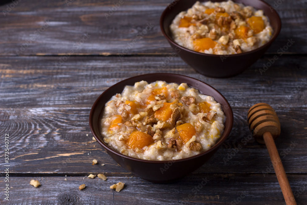 Delicious oatmeal porridge with baked pumpkin, honey and nuts in ceramic bowl on wooden table. healthy homemade breakfast. selective focus, space